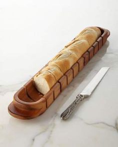 a loaf of bread sitting in a wooden container next to a knife on a marble counter