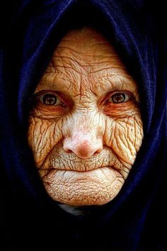 an old woman with wrinkles on her face and hood over her head is looking at the camera