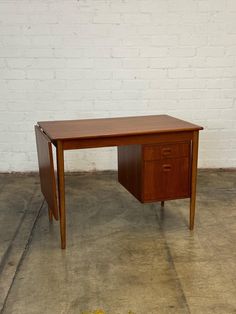 a wooden desk sitting on top of a cement floor next to a white brick wall