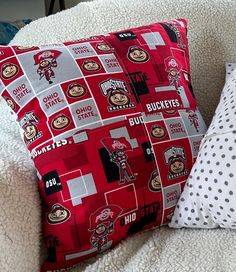 two pillows sitting on top of a couch covered in red and white fabric with football logos