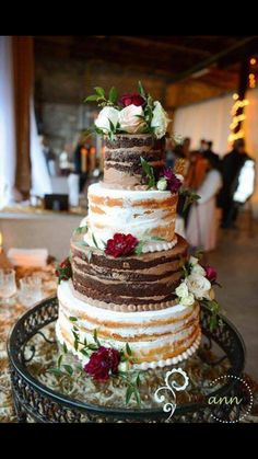 a three tiered cake with flowers and greenery on top sits on a table