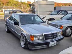 two mercedes benzs are parked next to each other in a parking lot, one is silver and the other is black