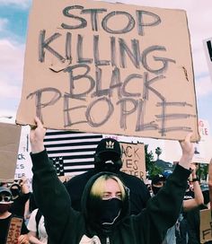 a protester holds up a sign that reads stop killing black people, while wearing a mask