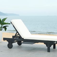 a lounge chair sitting on top of a stone patio next to the ocean with a potted plant in front of it