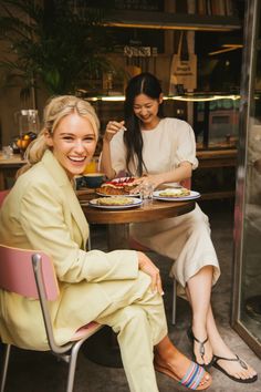 two women sitting at a table with plates of food in front of them and smiling