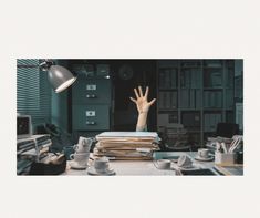 a stack of books and papers on a desk with a hand reaching out from the top