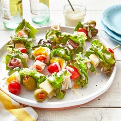 a white plate topped with lettuce and tomato skewers on top of a table