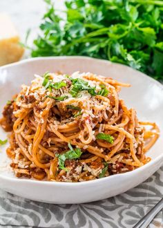 a white bowl filled with spaghetti and meat on top of a table next to parsley