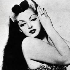 a black and white photo of a woman holding her hair up to her face with one hand