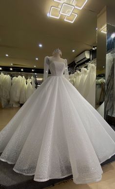 a white wedding dress is on display in a clothing store with mannequins behind it