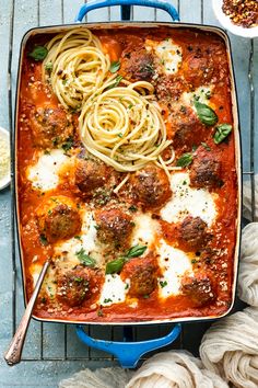 a blue casserole dish filled with meatballs and pasta, garnished with parmesan cheese