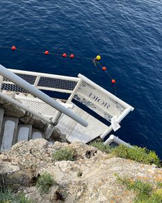 a white bench sitting on top of a cliff next to the ocean with red and yellow balls hanging from it