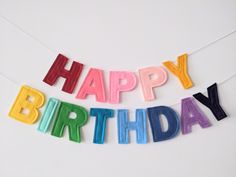 the word happy birthday spelled with colorful letters on a white background, hanging from a string