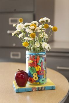 a vase filled with flowers and letters on top of a table next to an apple