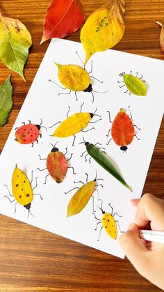 a child's hand is holding a marker over a paper with leaves and ladybugs on it