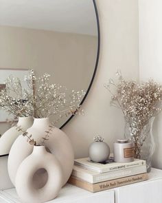 a white vase with flowers on top of a dresser next to a mirror and books