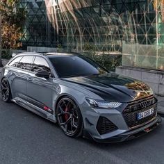 a grey car parked in front of a large glass building on the side of a street