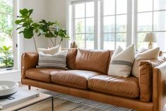 a brown leather couch sitting in front of a window next to a table with a bowl on it