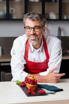 a man with glasses and an apron standing in front of a cupcake on a counter