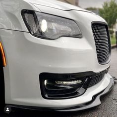 the front end of a white car with chrome rims and an orange brake light