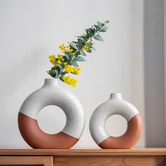 two white and brown vases sitting on top of a wooden shelf next to yellow flowers