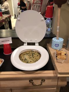 a white toilet sitting on top of a wooden counter next to bowls of food and drinks