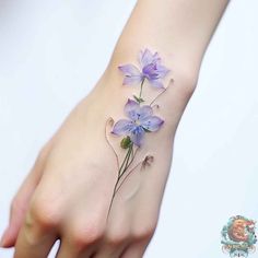 a woman's hand with purple flowers tattooed on the left side of her wrist