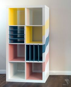 a multicolored bookcase is against a white wall