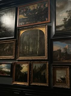 many paintings are hanging on the wall next to each other in a room with dark walls