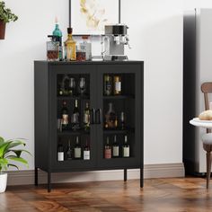 a black cabinet with wine glasses and bottles on it next to a white chair in front of a potted plant