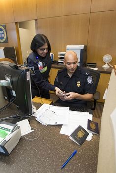 two police officers sitting at a desk looking at their cell phones and paperwork on the table