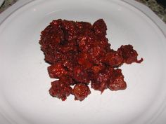 a white plate topped with red food on top of a marble countertop next to a knife and fork