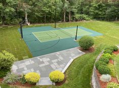 an aerial view of a tennis court surrounded by lush green grass and trees with basketball hoop in the middle