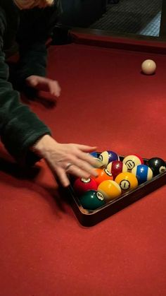 a person reaching for a pool ball in a pool table with several balls on it