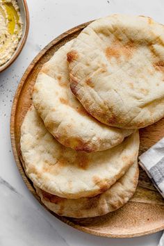 four pita breads on a wooden plate next to a bowl of hummus