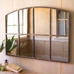 a mirror hanging on the side of a wall next to a wooden table and plant