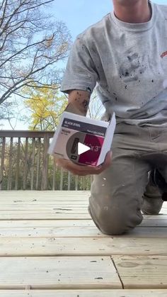 a man kneeling down on a deck holding a box with something in it and smiling at the camera