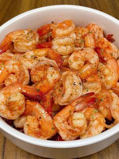 a white bowl filled with cooked shrimp on top of a wooden table