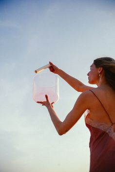 a woman in a red dress is holding a plastic jug and looking up into the sky