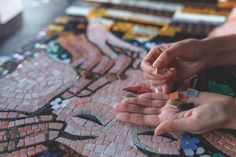 two hands are holding small pieces of glass mosaic tile