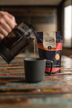 a person pouring coffee into a bag on top of a table next to a cup