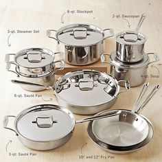 an assortment of stainless steel pots and pans on a wooden table with utensils