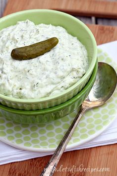 a green bowl filled with dip and a pickle sitting on top of it next to a spoon