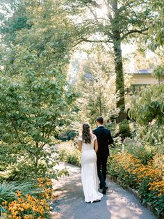 a bride and groom walking down a path in the woods