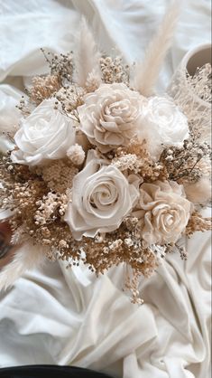 a bridal bouquet with white roses and feathers on a bed sheet in the sunlight