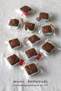 small chocolates wrapped in plastic sitting on top of a white tablecloth with the words mini brownies next to them