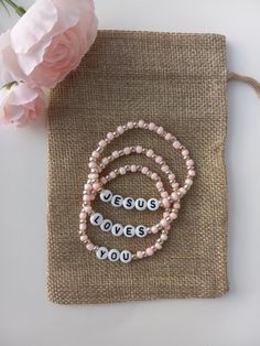 three bracelets with words on them sitting next to a pink flower and burlock