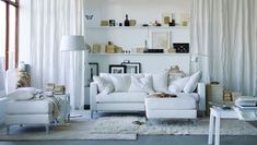 a living room filled with white furniture and lots of books on the shelf above it