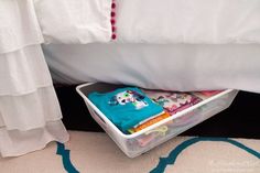 a bed with white sheets and a plastic basket under it