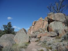 some big rocks and trees on the side of a hill with blue skies in the background